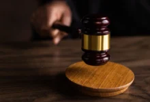 Ahşap masa üzerinde altlığına doğru tutulan hakim tokmağı.
